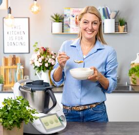 Dési steht neben dem Thermomix® und hält einen Teller Suppe