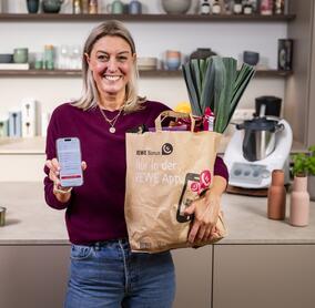 Dési vom ZauberTopf Club mit einer Einkaufstüte voller Lebensmittel von REWE