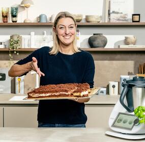 Blonde Frau mit einem Blech Kuchen neben dem Thermomix®