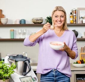 Blonde Frau in einer Küche neben dem Thermomix®, in der Hand eine Schale mit Nicecream