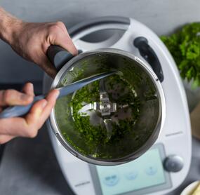 Blick in den Mixtopf des Thermomix®, darin sind zerkleinerte Kräuter