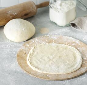 Ausrerollter Pizzateig auf einem Holzbrett