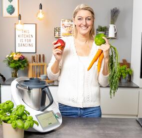 Désiree steht vor dem Thermomix® und hält Gemüse hoch
