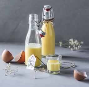 Zwei Flaschen mit Eierlikör, daneben ein Glas mit dem gelben Likör und Eierschalen
