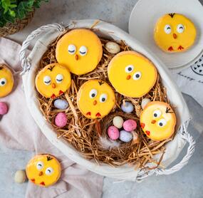 Auflaufform mit Stroh und bunten Mini-Eiern, darin liegen die als Küken verziehrten Amerikaner