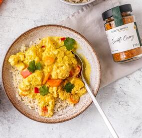 Sweet Curry Gewürz in einem Glas neben einem Teller mit einem Curry-Gericht