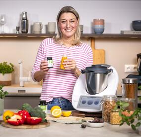 Blonde Frau mit einem Thermomix® und einem Glas mit Eisen-Tabletten