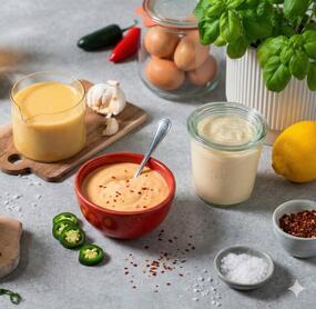 Mehrere Gläser und Schalen mit Soßen, daneben Eier, Salz, Kräuter, Ölflaschen