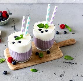 Zwei Smoothies, unten lila, oben weiß, mit Strohhalmen