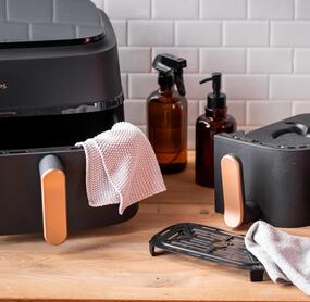 Airfryer in Einzelteilen, daneben Putzspray und Lappen