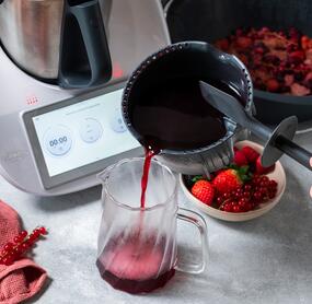Jemand gießt Saft aus dem Simsafix® Einsatz für Thermomix® in eine Karaffe