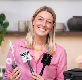 Blonde Frau mit mehreren Spülbürsten in einer Hand