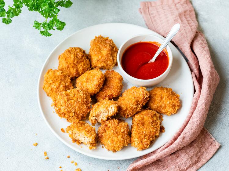 Chicken Nuggets mit Cornflakes-Panierung auf rundem Teller mit Ketchup in Schälchen